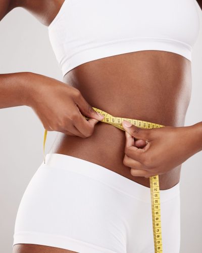 Tape measure, waist and stomach or body of woman for health and wellness on studio background. Fitn.